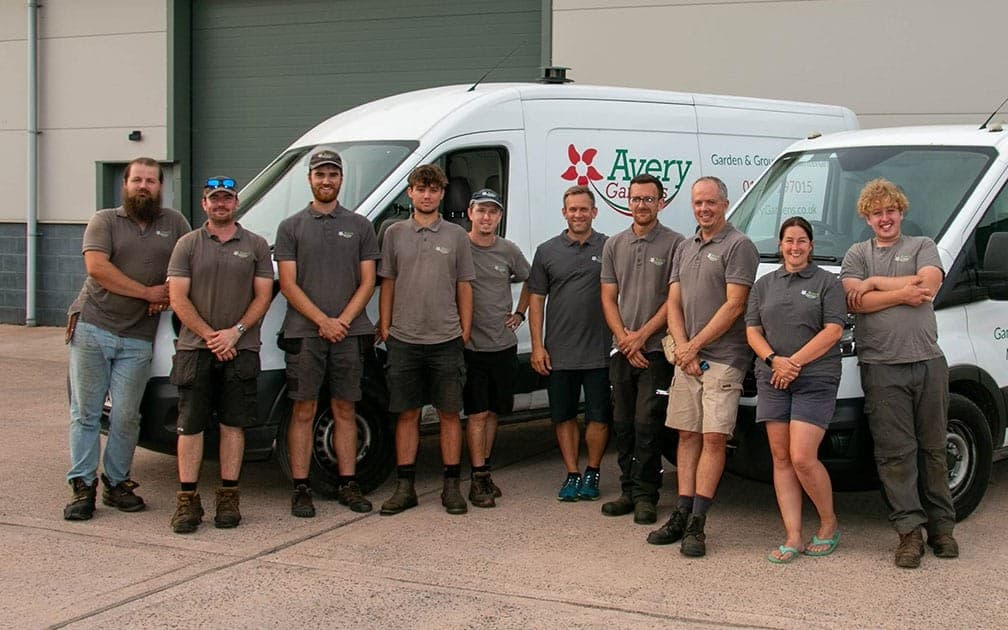 The Avery grounds maintenance team standing together in branded polo shirts in front of two company vans